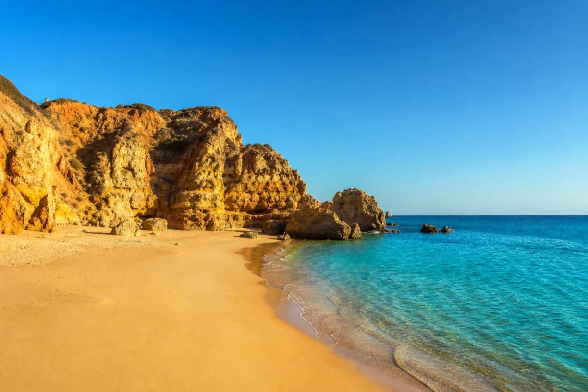 Klippinramad sandstrand med turkost atlantvatten längs Algarves sydkust i Portugal