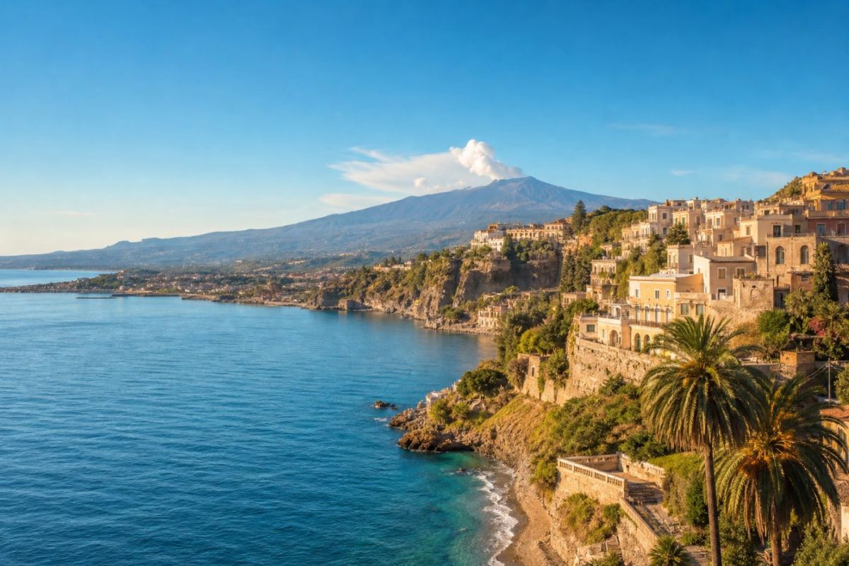 Solig kustvy över Catania med havet i förgrunden och en rykande vulkan i bakgrunden