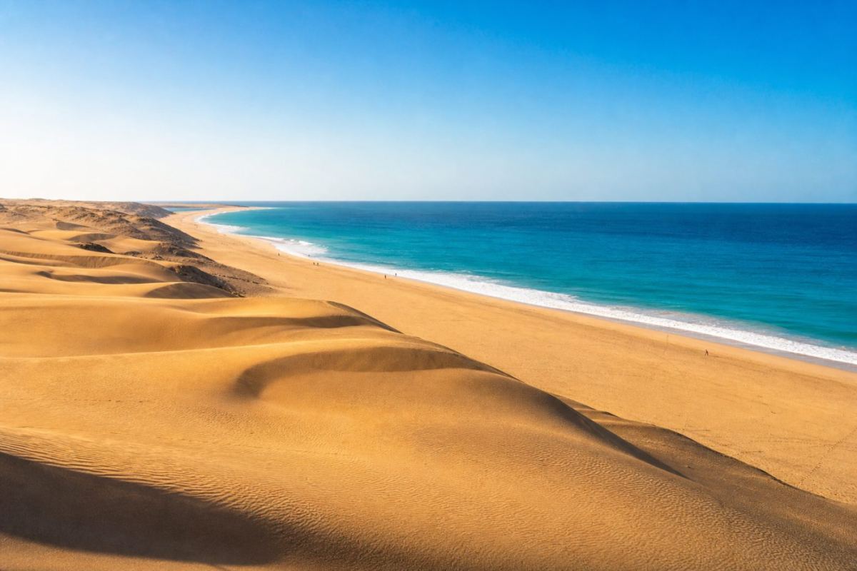 Gyllene sanddyner som möter en lång sandstrand och turkost hav på Gran Canaria en solig dag