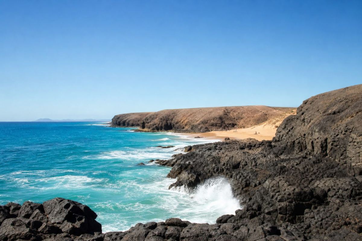 Svart vulkanisk lavakust som möter glittrande blått hav under klar himmel på Lanzarote