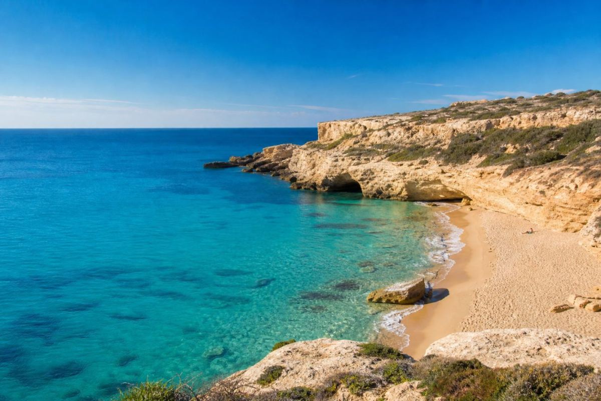 Solbelyst klippkust med turkost medelhavsvatten och en liten badvik på Malta
