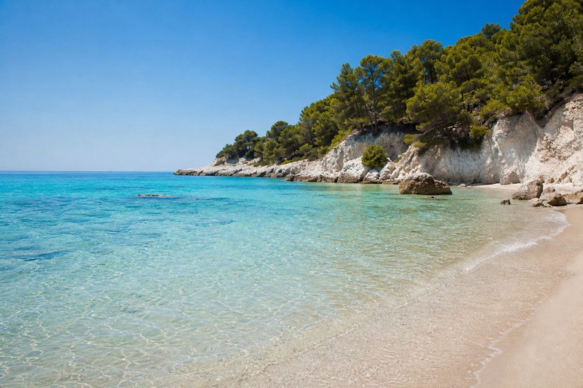 Solig sandstrand med turkost vatten och kalkstensklippor på Menorca i Spanien