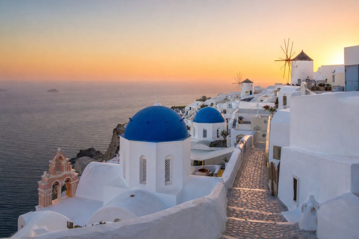 Vitkalkade hus med blå kupoler och väderkvarnar ovanför ett turkost Egeiska hav på Mykonos i solnedgång