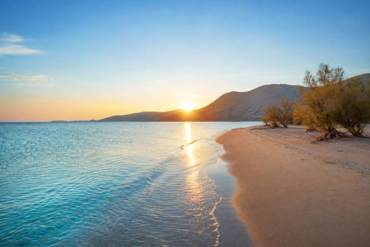 Soluppgång över en lång sandstrand på Naxos med turkost grunt vatten och kala kykladiska berg i fjärran