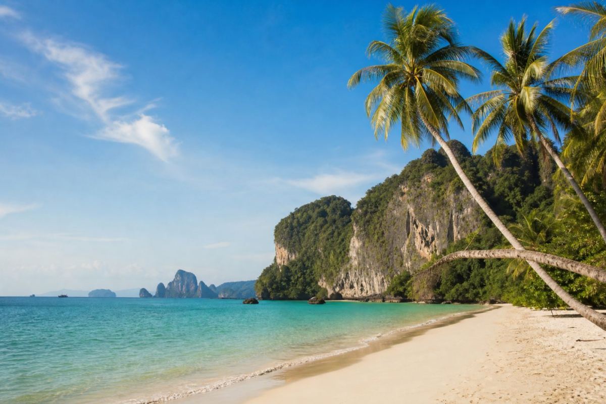 Lång vit sandstrand med kalkstensklippor och turkost vatten i tropiska Thailand